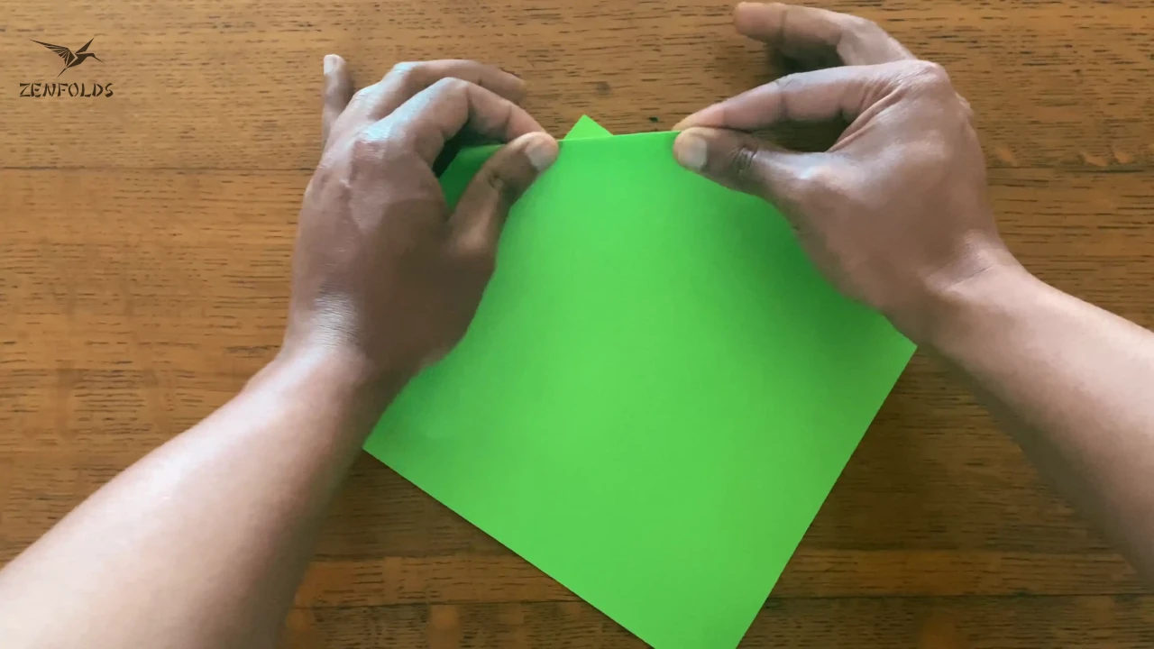 a mountain fold being creased on a square origami sheet